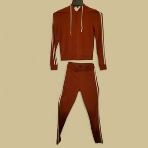 A rust colored 2-piece tracksuit with white stripes down the sides of the arms